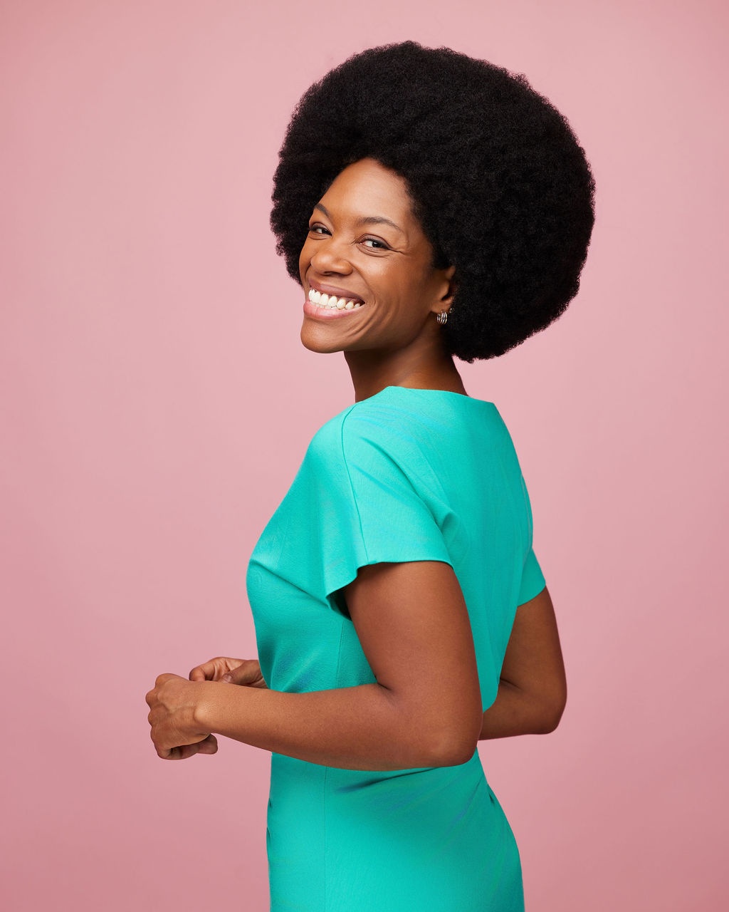 Sabrina smiling in a studio portrait with a voluminous Afro against a soft pink backdrop
